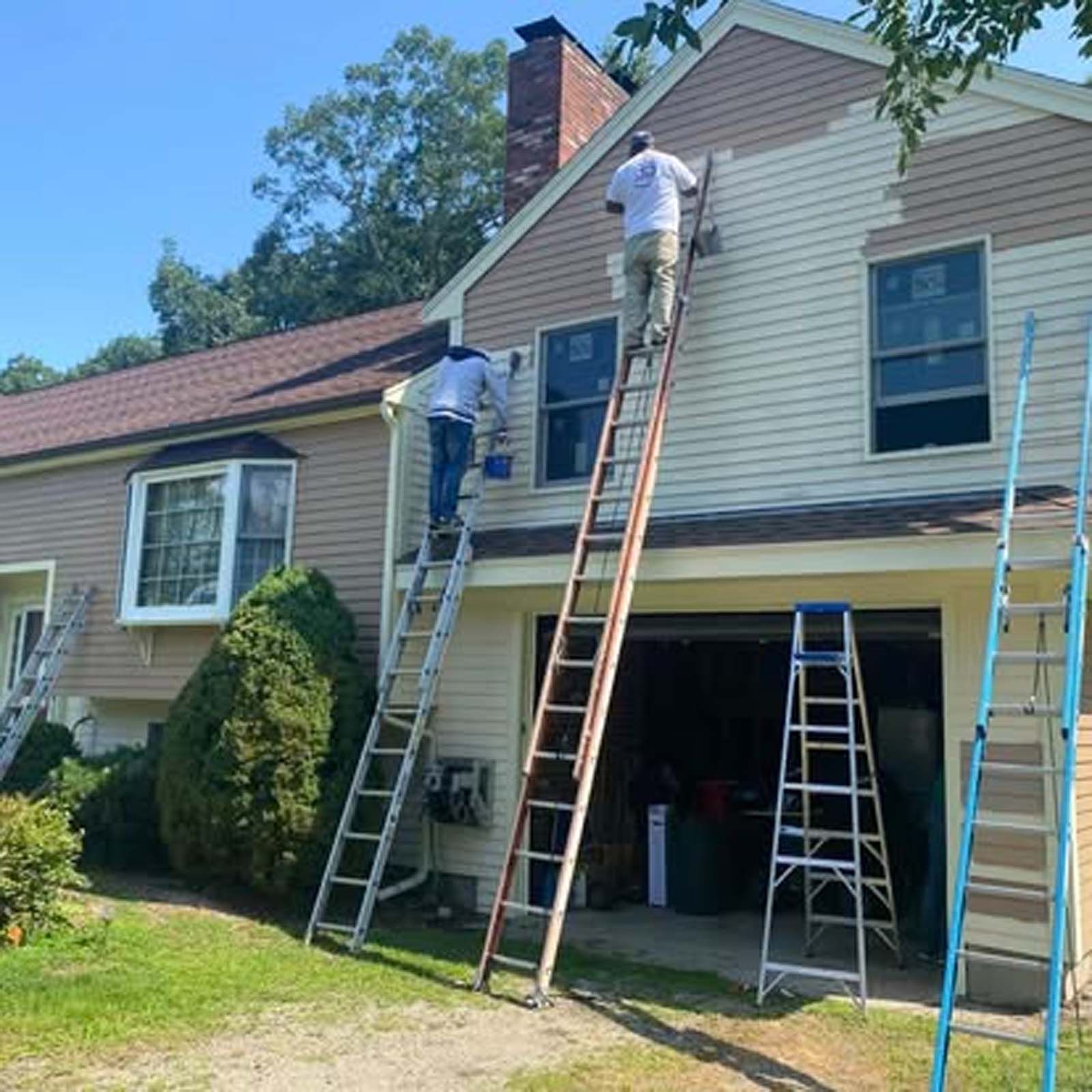 Two men are painting the side of a house with ladders