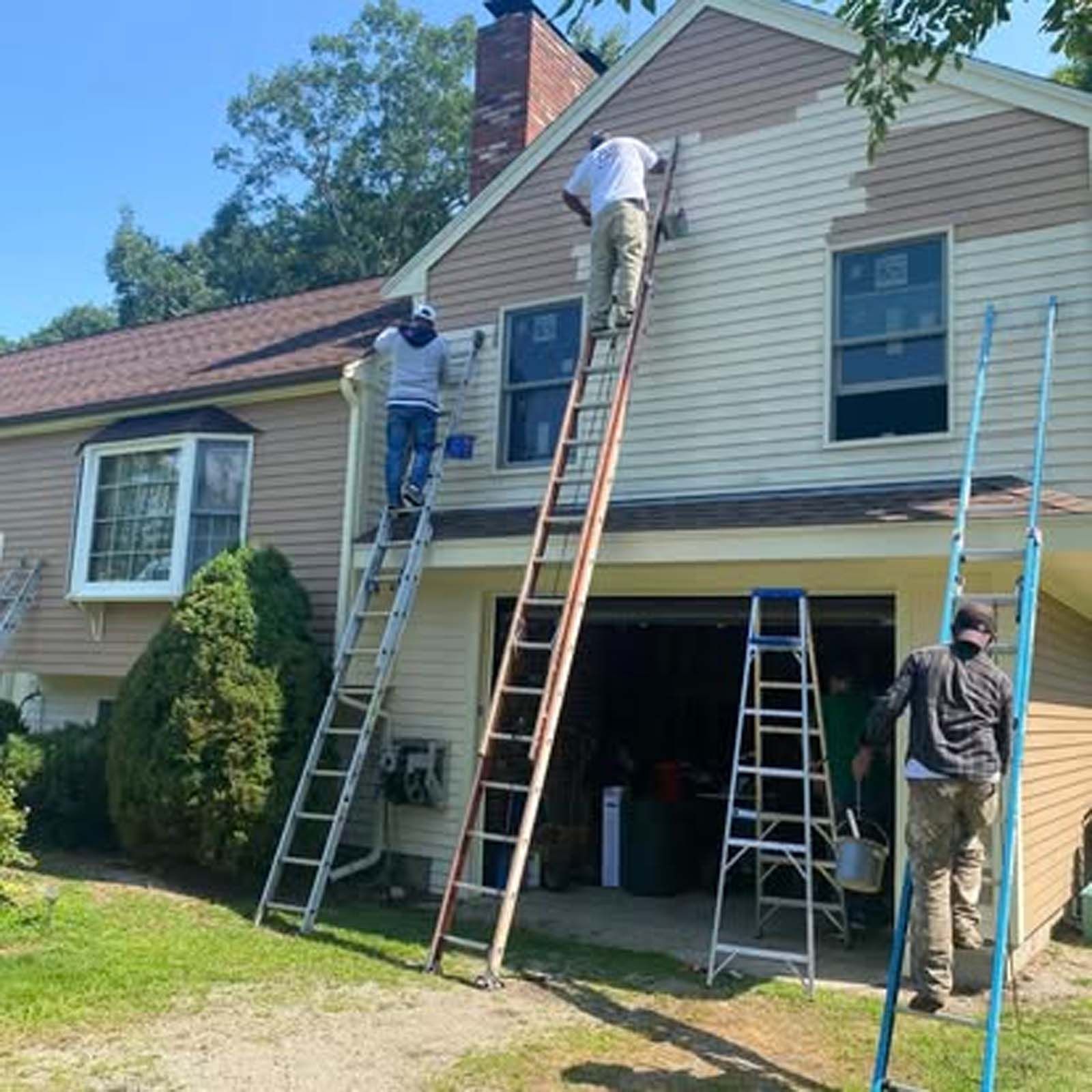 Two men are painting the side of a house with ladders