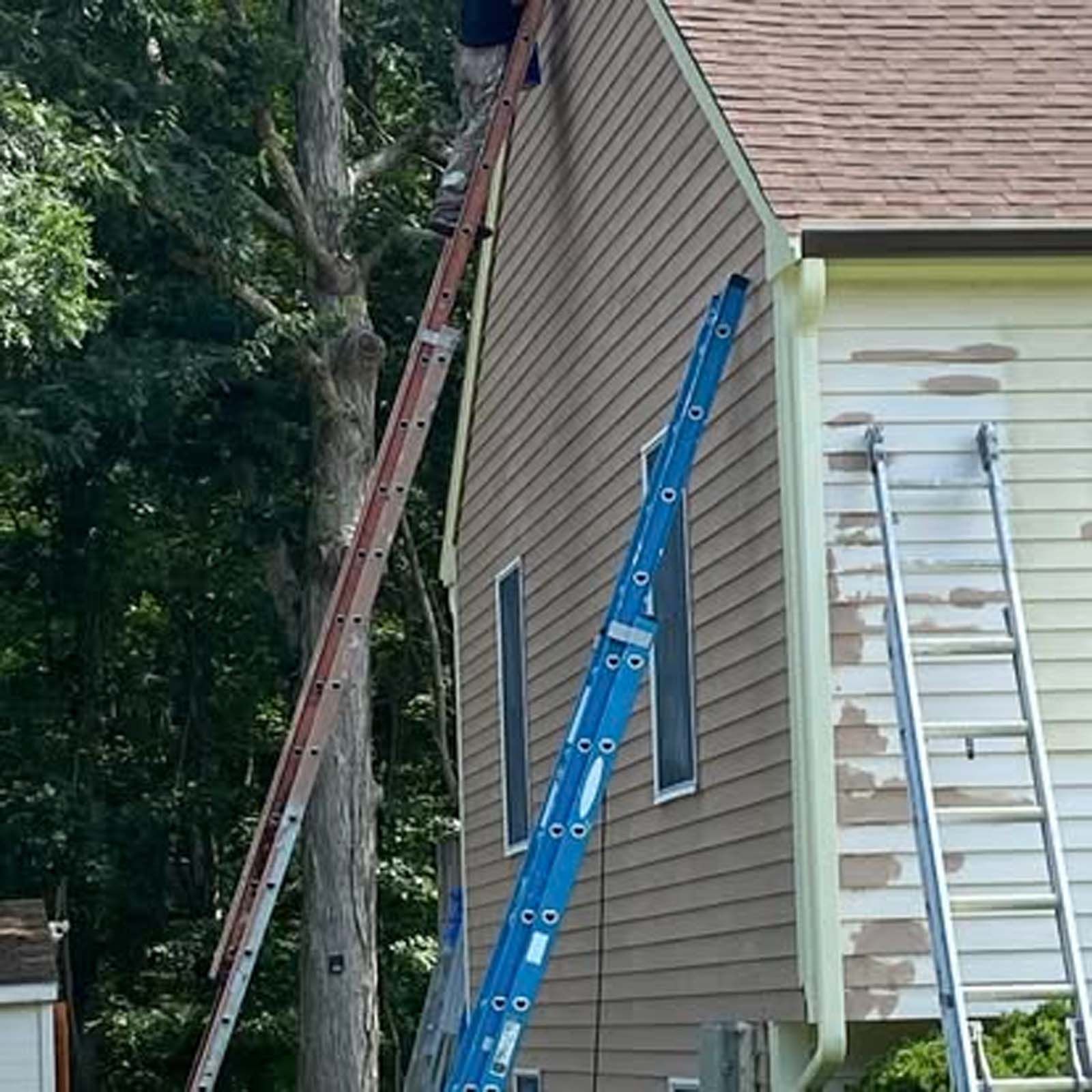 A man is standing on a ladder on the side of a house