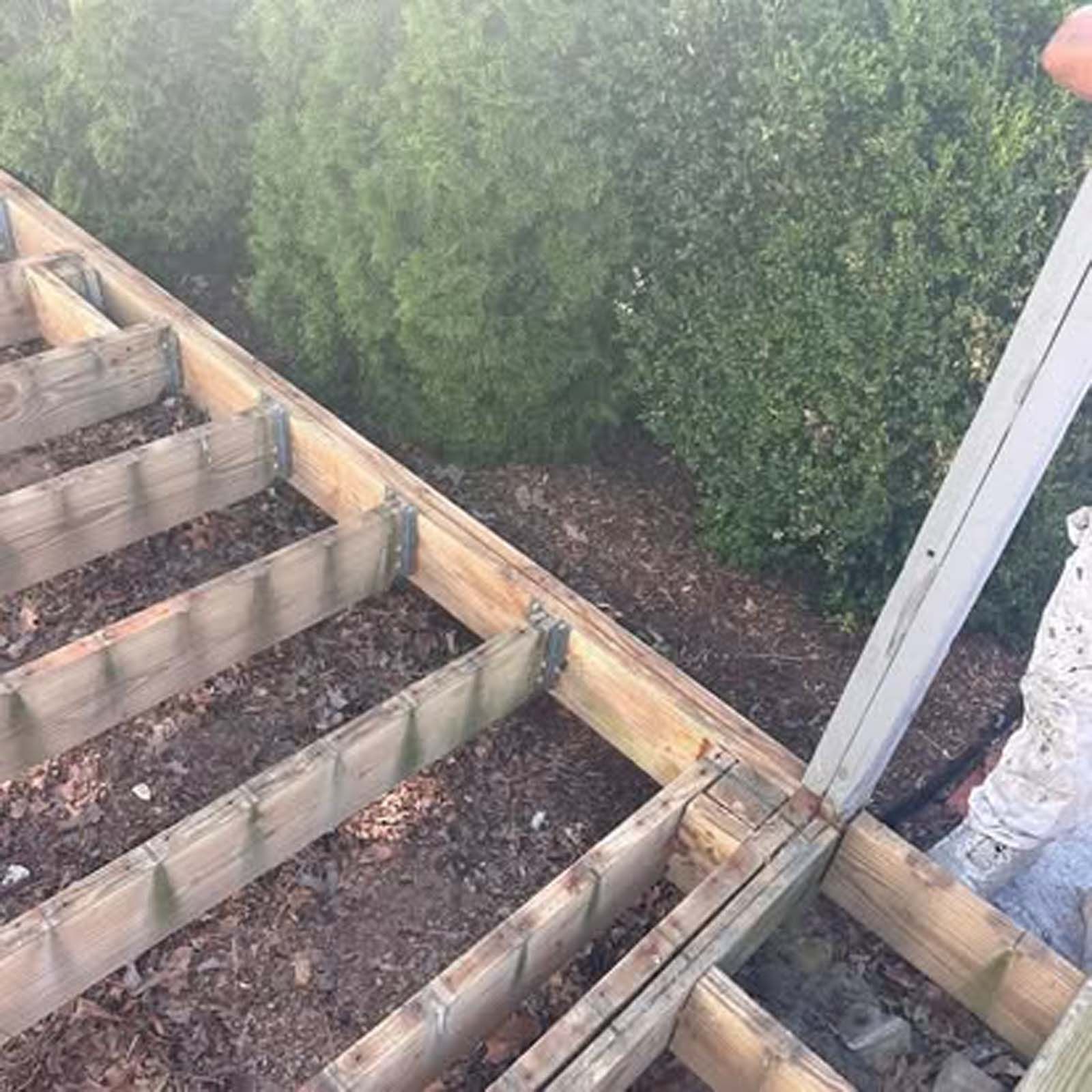 A person is working on a wooden deck with trees in the background.