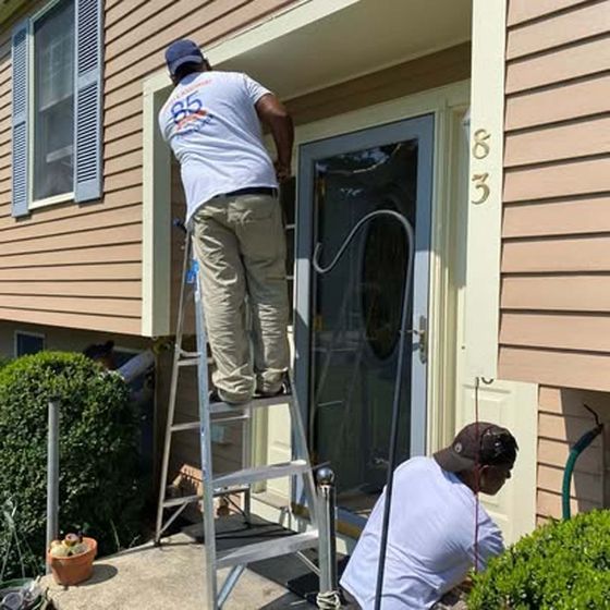 Two men are working on the front door of a house.