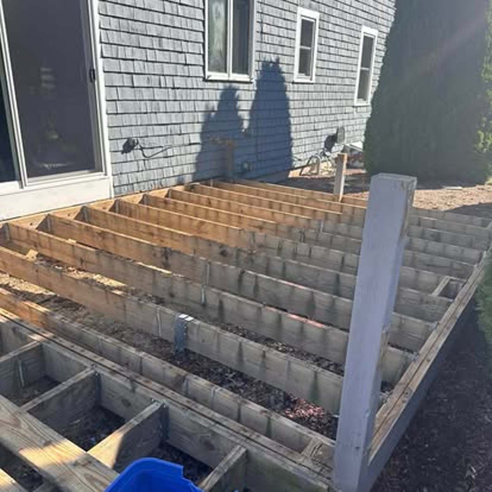 A wooden deck is being built in front of a brick house.