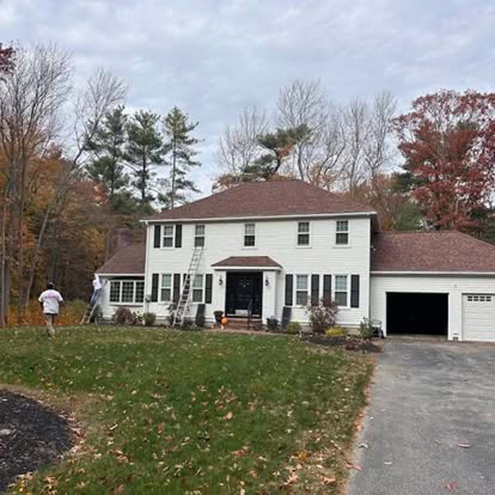 A large white house with a brown roof is being painted.