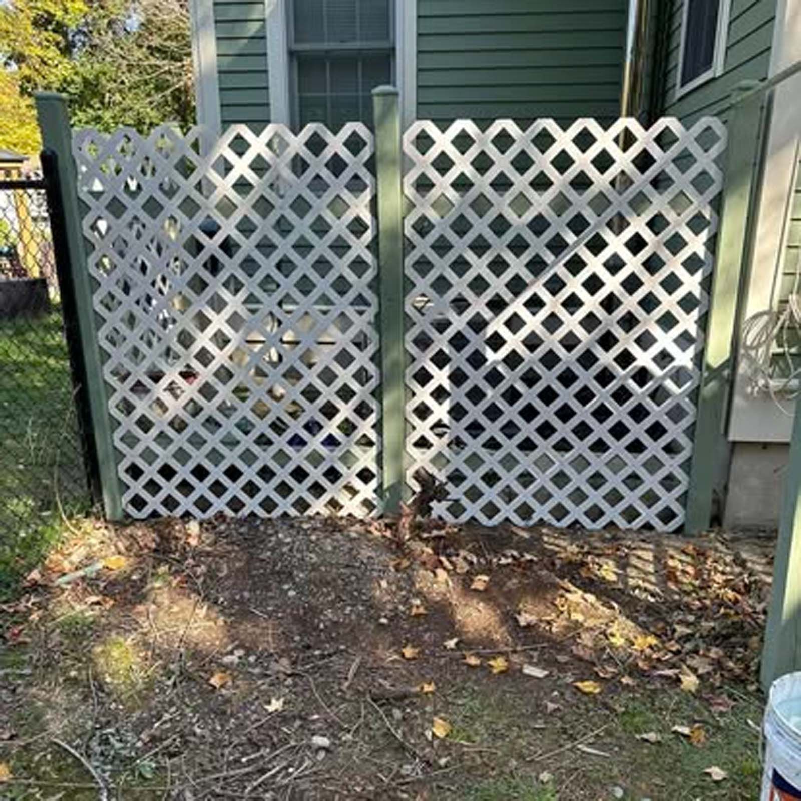 A white lattice fence is sitting in front of a green house.