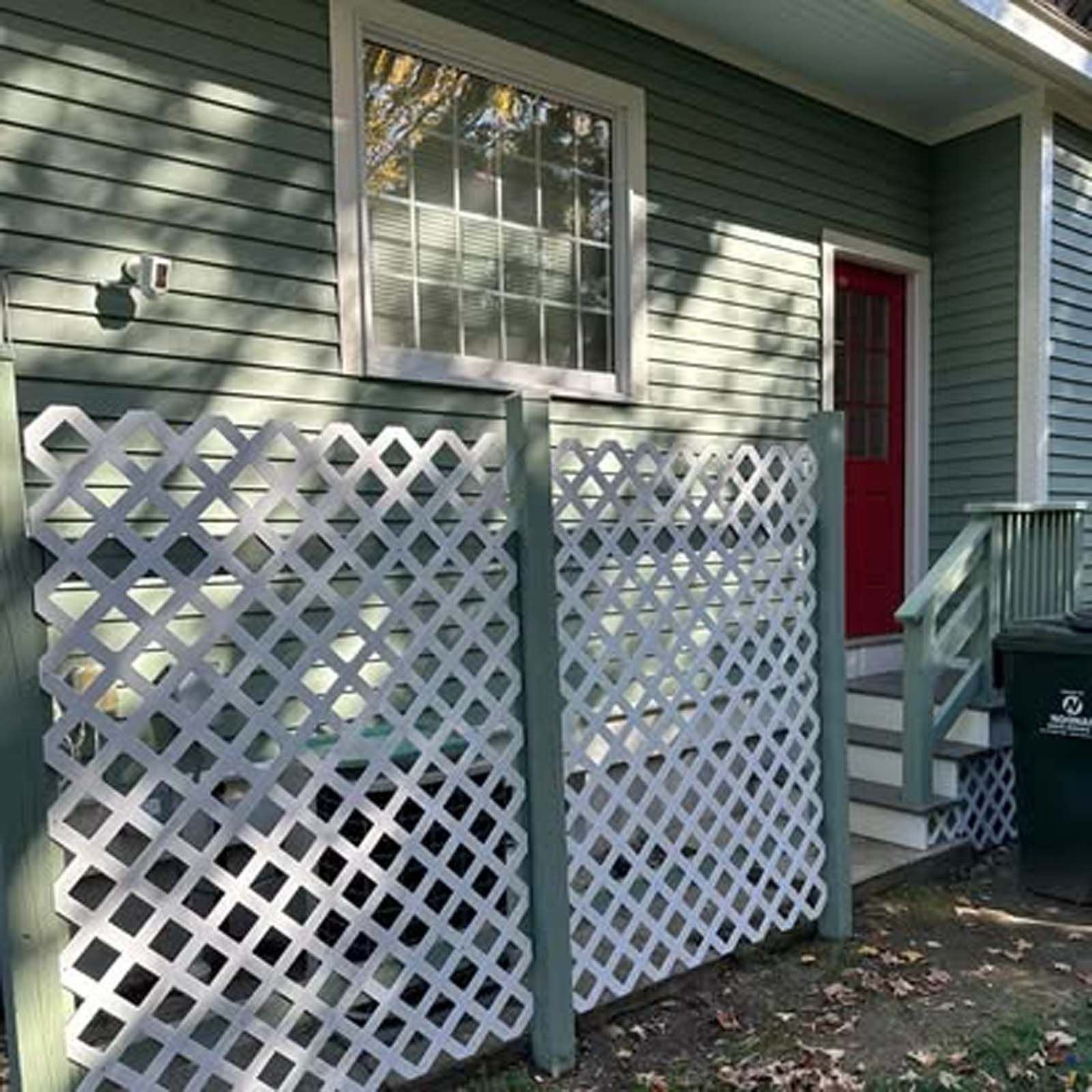 A green house with a white lattice fence and a red door.