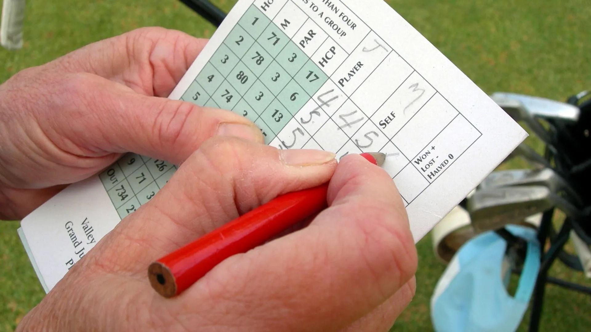 A person is writing on a golf scorecard with a red pencil