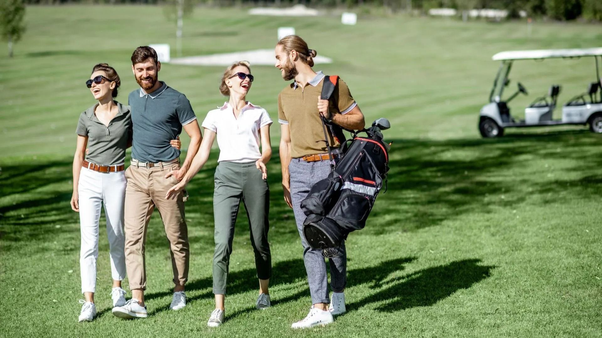 A group of people are standing on a golf course with a golf cart in the background.