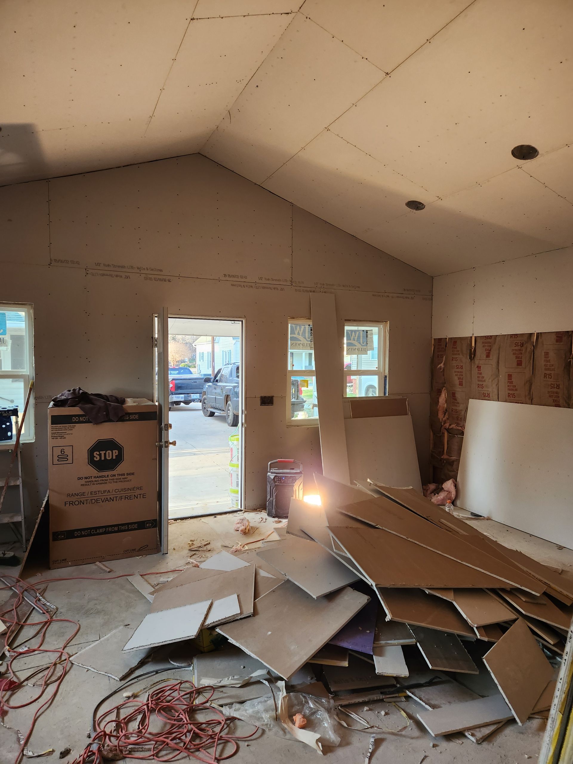 Interior construction, drywall installation in progress. Room with open doorway, debris on floor.