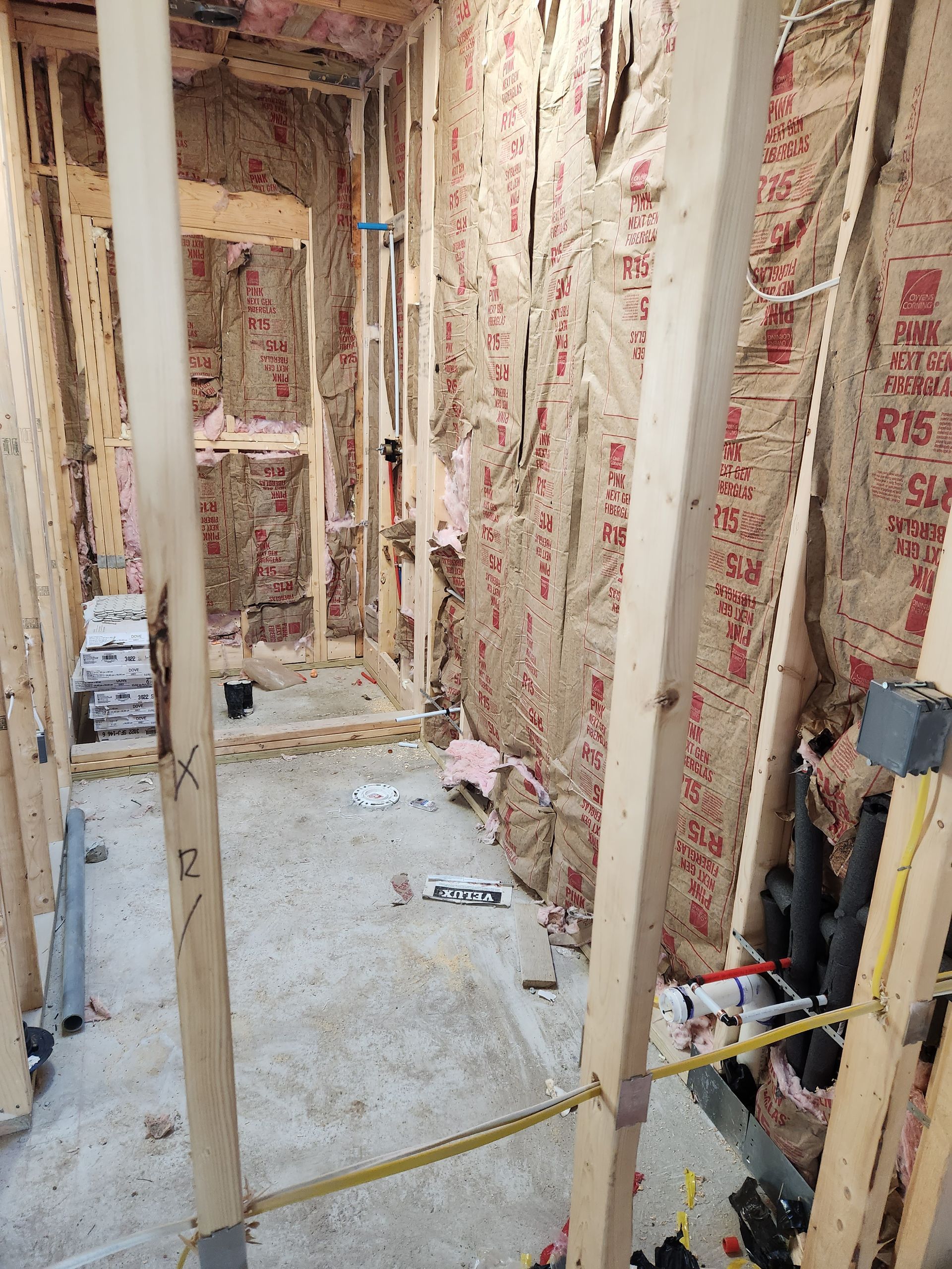 Interior view of a bathroom under construction, showing wooden framing, insulation, and plumbing.