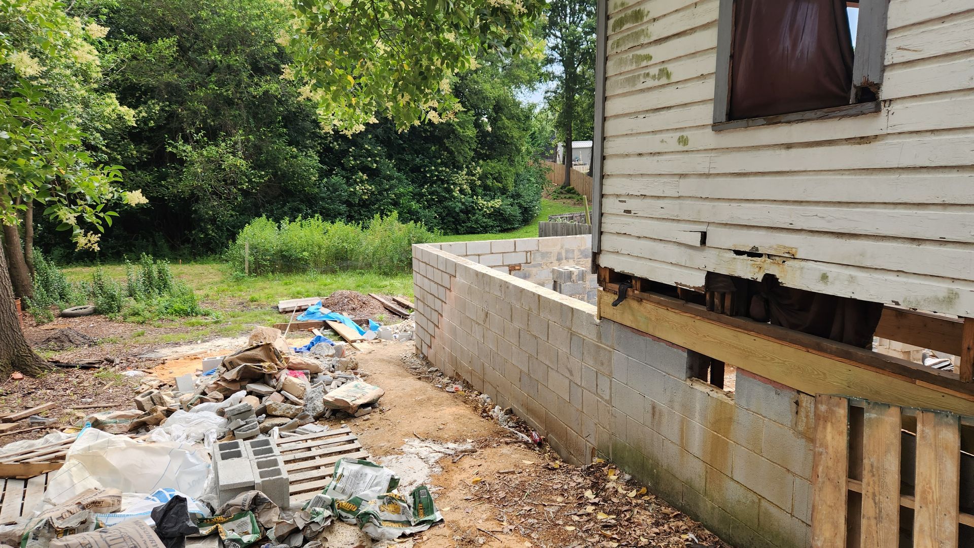 Dilapidated house, wooden siding, concrete foundation, debris in yard, overgrown vegetation.