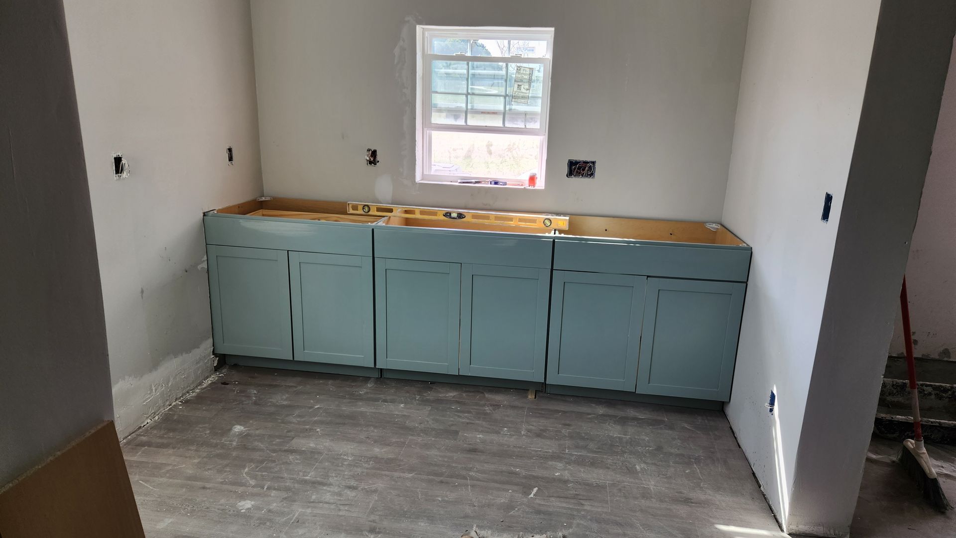 Room under construction with blue cabinets, a small window, and gray flooring.