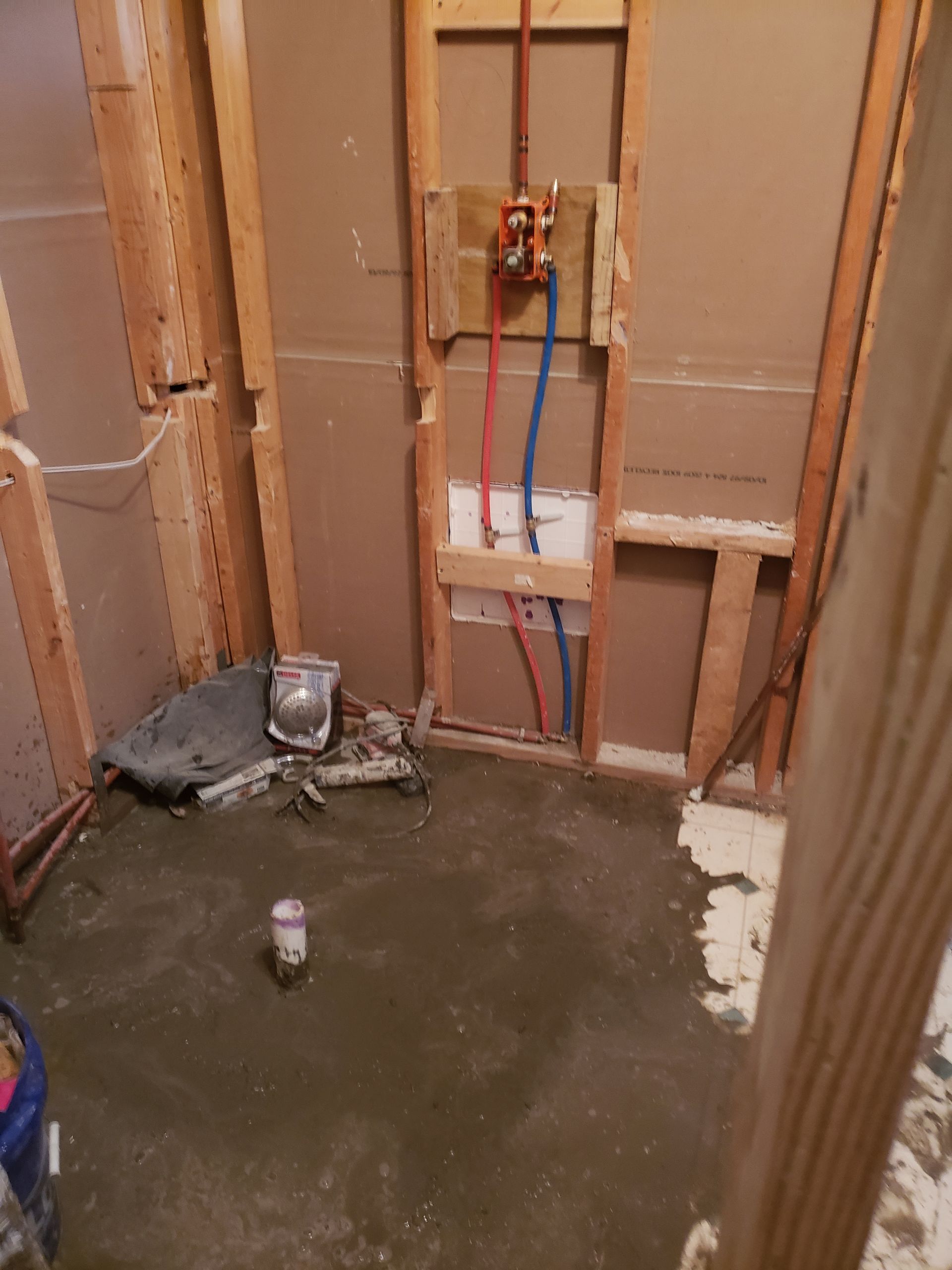 Bathroom under construction with exposed framing, plumbing, and concrete floor.