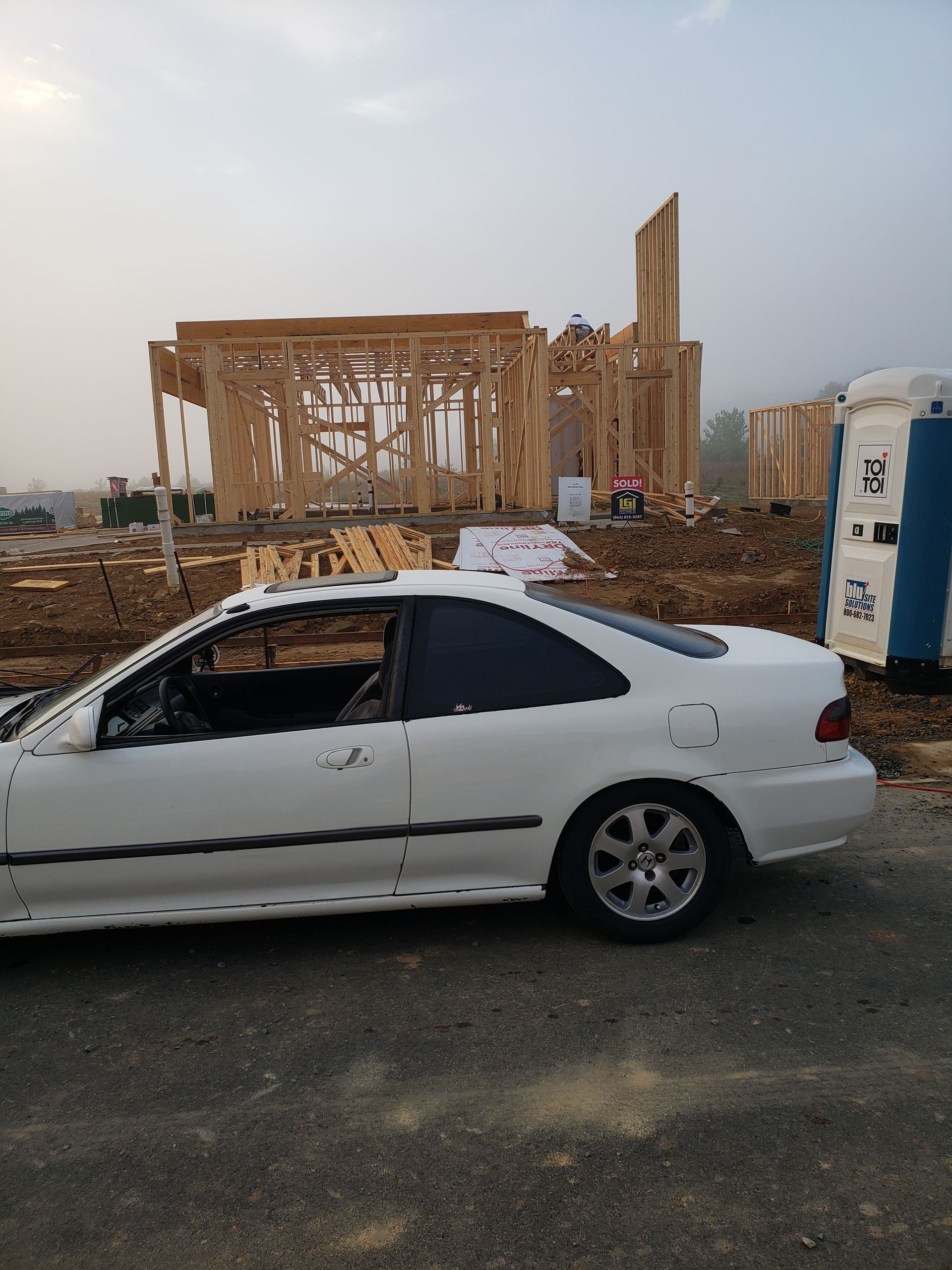 White car parked near a house under construction; cloudy sky.