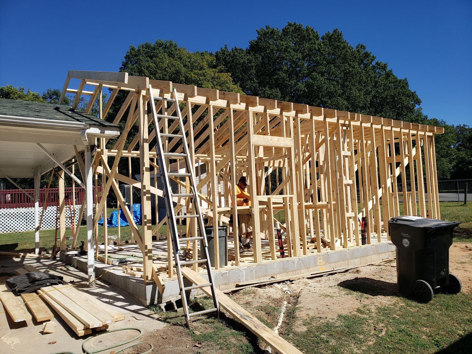 Wooden frame of a building under construction on a concrete foundation, with a ladder leaning against it.