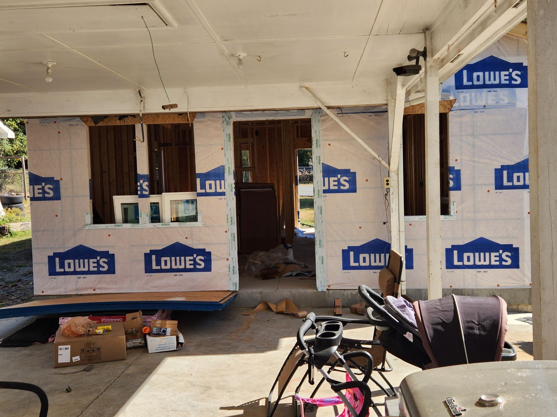 Exterior of a building under construction, with Lowe's wrap visible. Materials and tools on the porch.