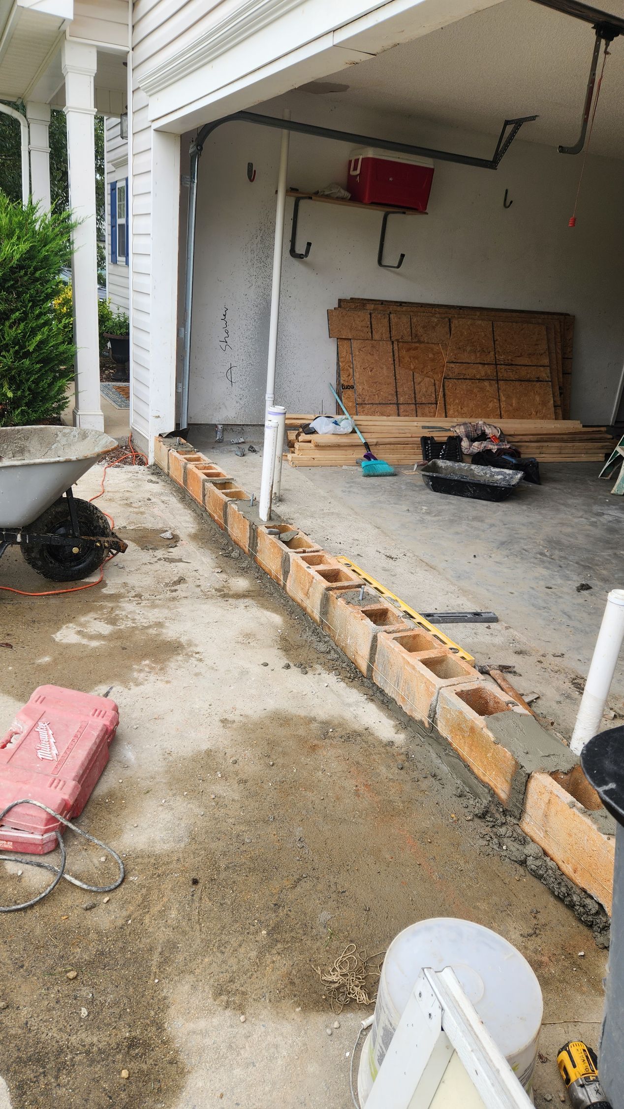 Construction site: cinder blocks outlining a low wall in front of a garage. Wet concrete, tools, and lumber present.