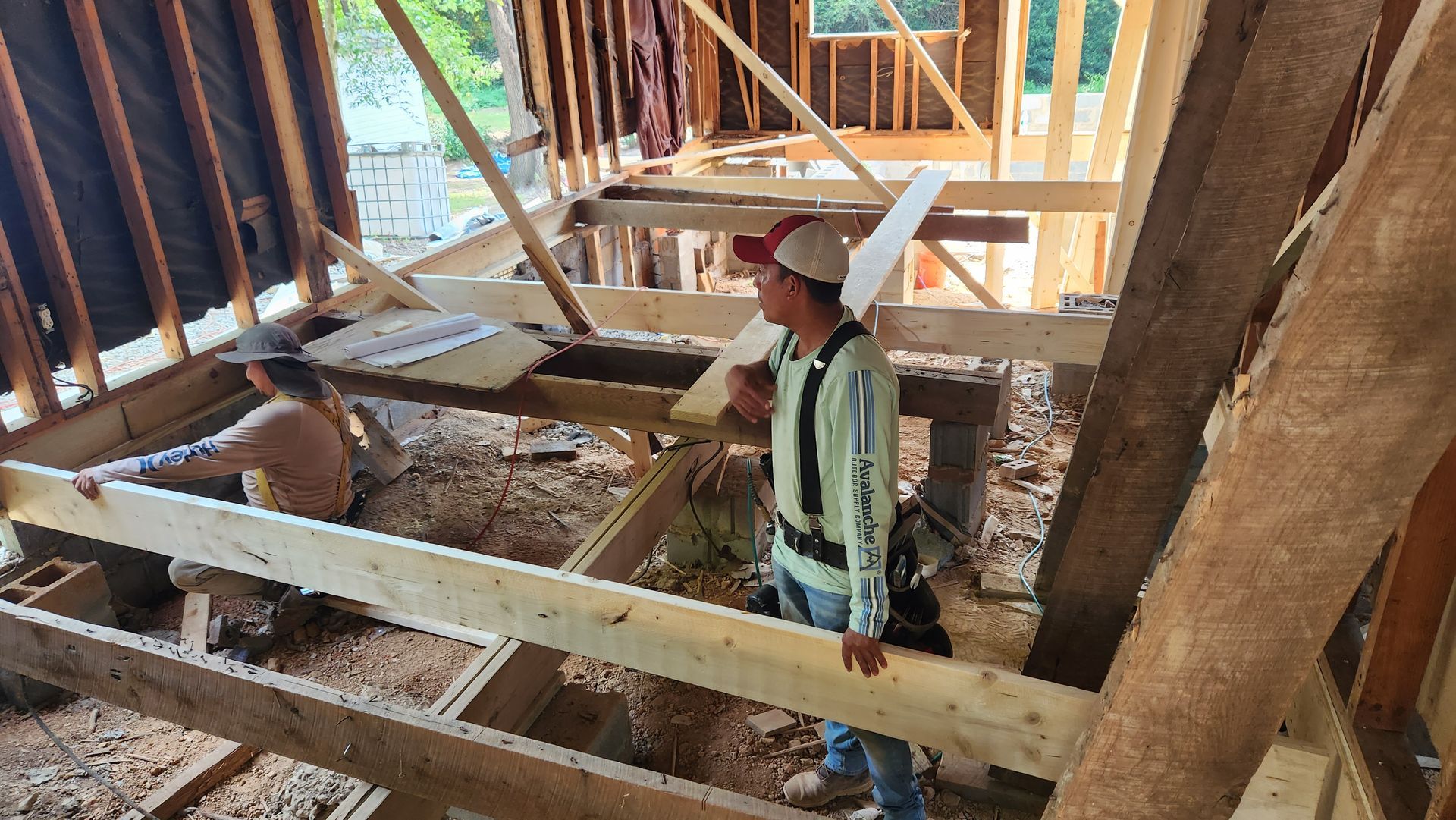 Two workers building wood framework inside a roof structure.  Daylight streams in, scattered debris below.