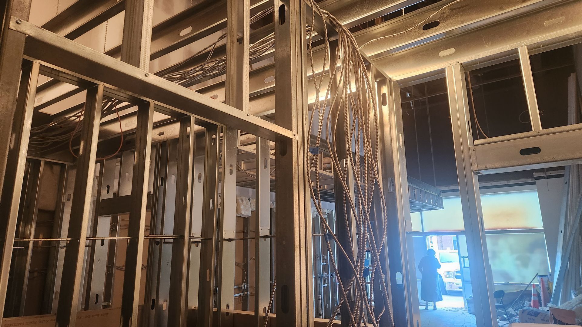 Interior construction: wooden wall framing, wires, and a partial view of a room with windows and a person.