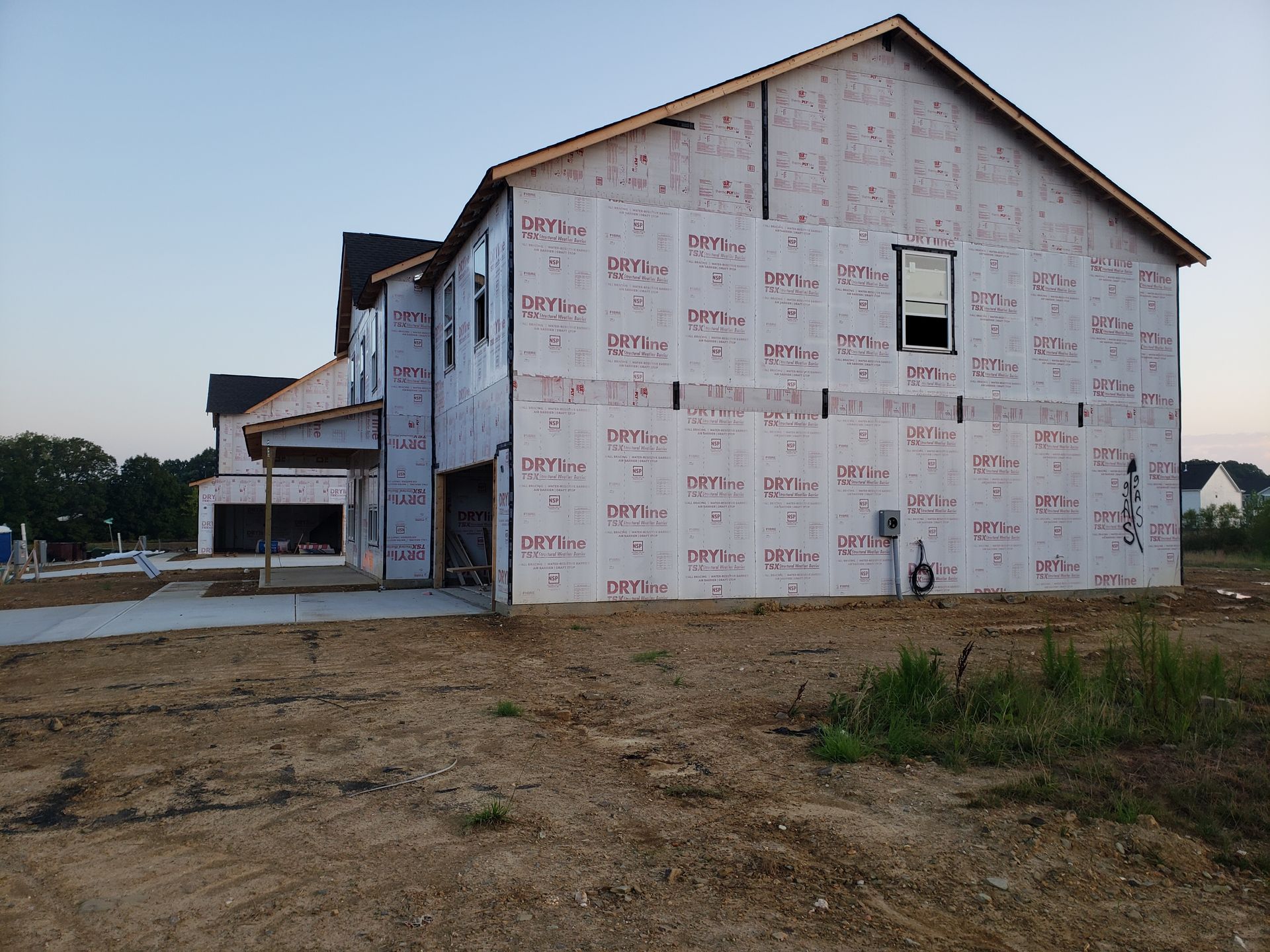 New house under construction, sheathed in red weather-resistant barrier, concrete driveway, and exposed framing.