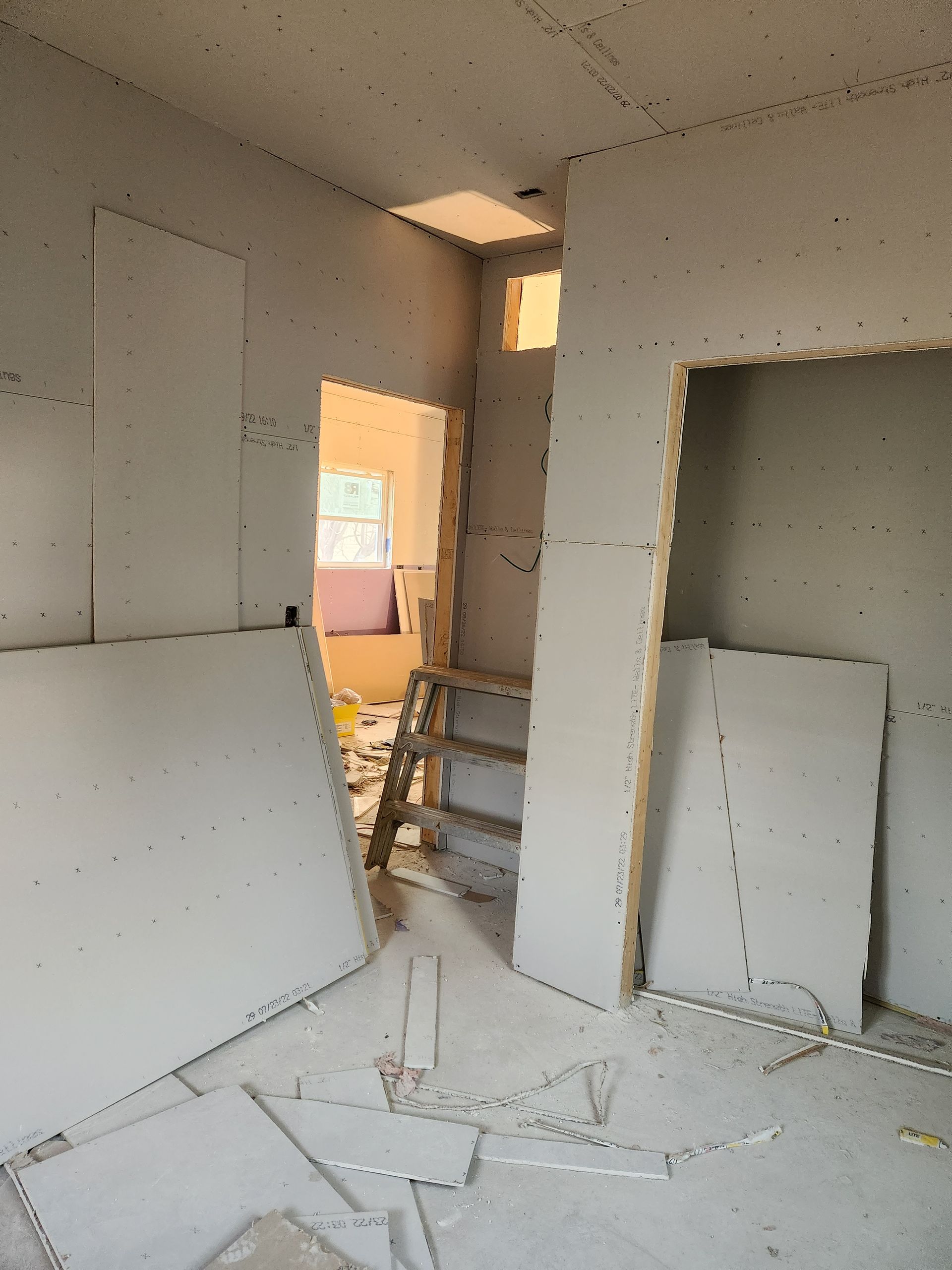 Interior construction: room with drywall partially installed, doorway, ladder, and debris on the floor.