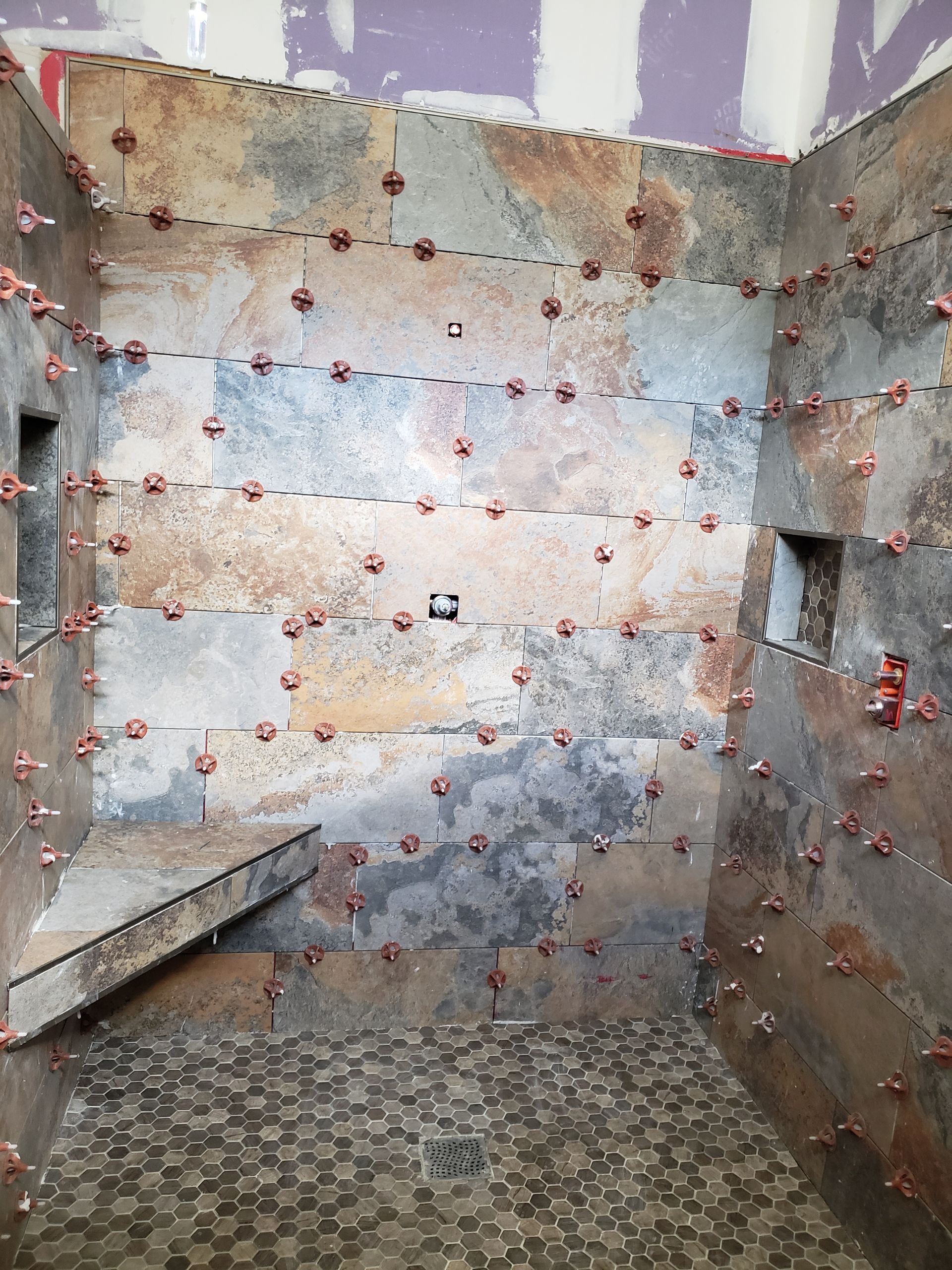 Bathroom shower with slate-like tile walls and pebble floor; red leveling clips are visible between the tiles.