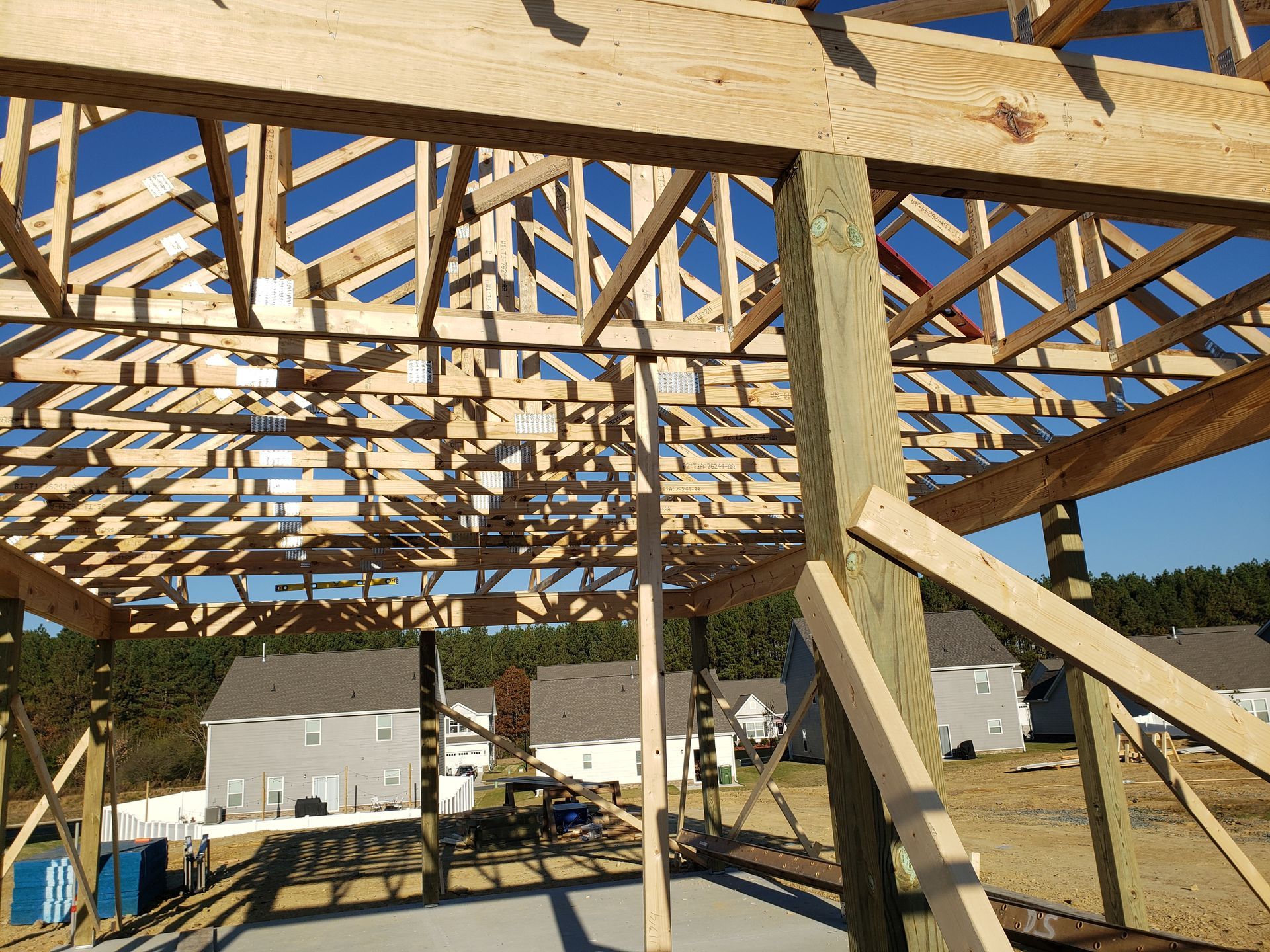 Wooden framing of a building under construction, with trusses and support beams against a blue sky.