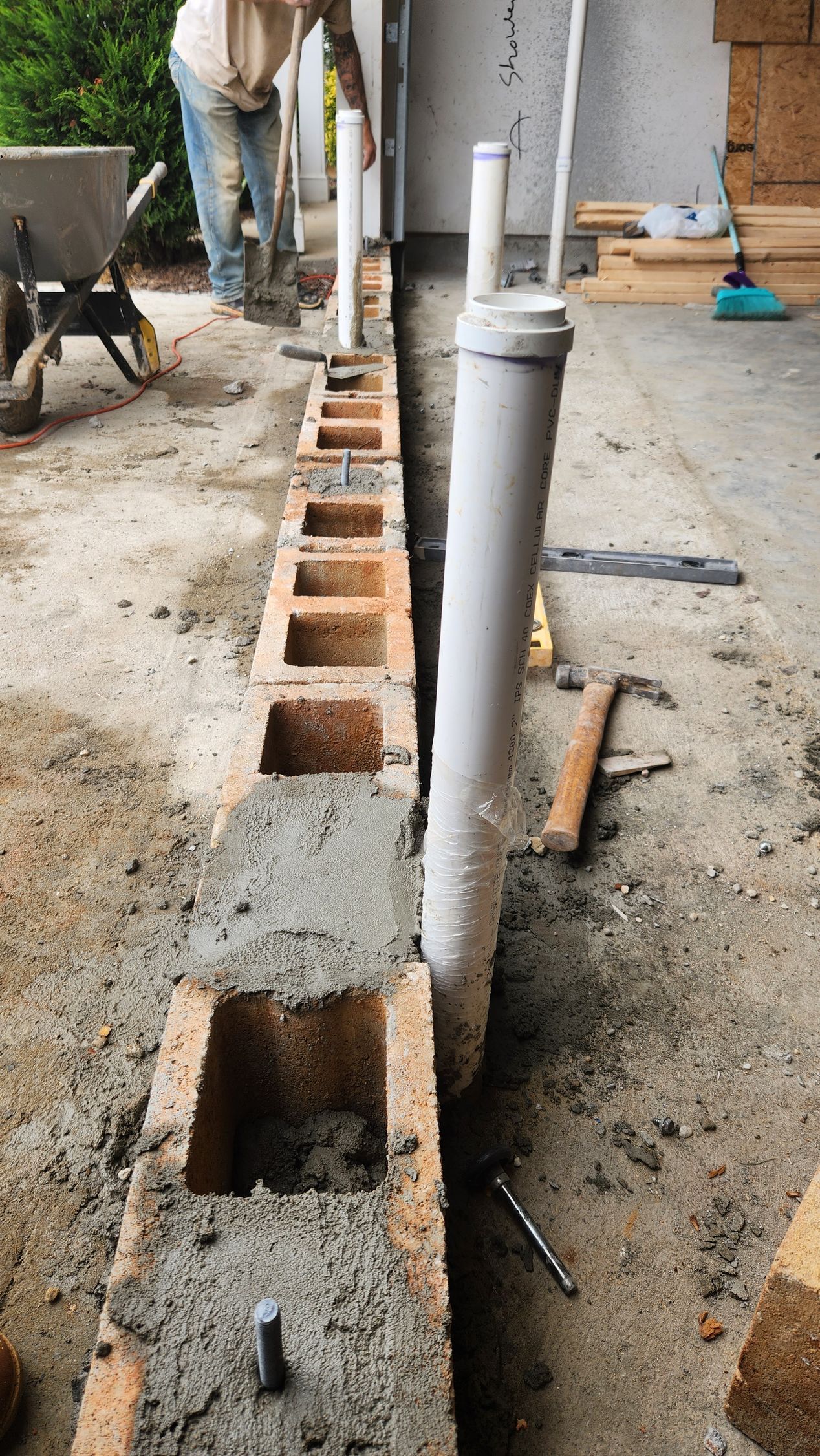 Construction of a brick wall with embedded pipes; a person is working.