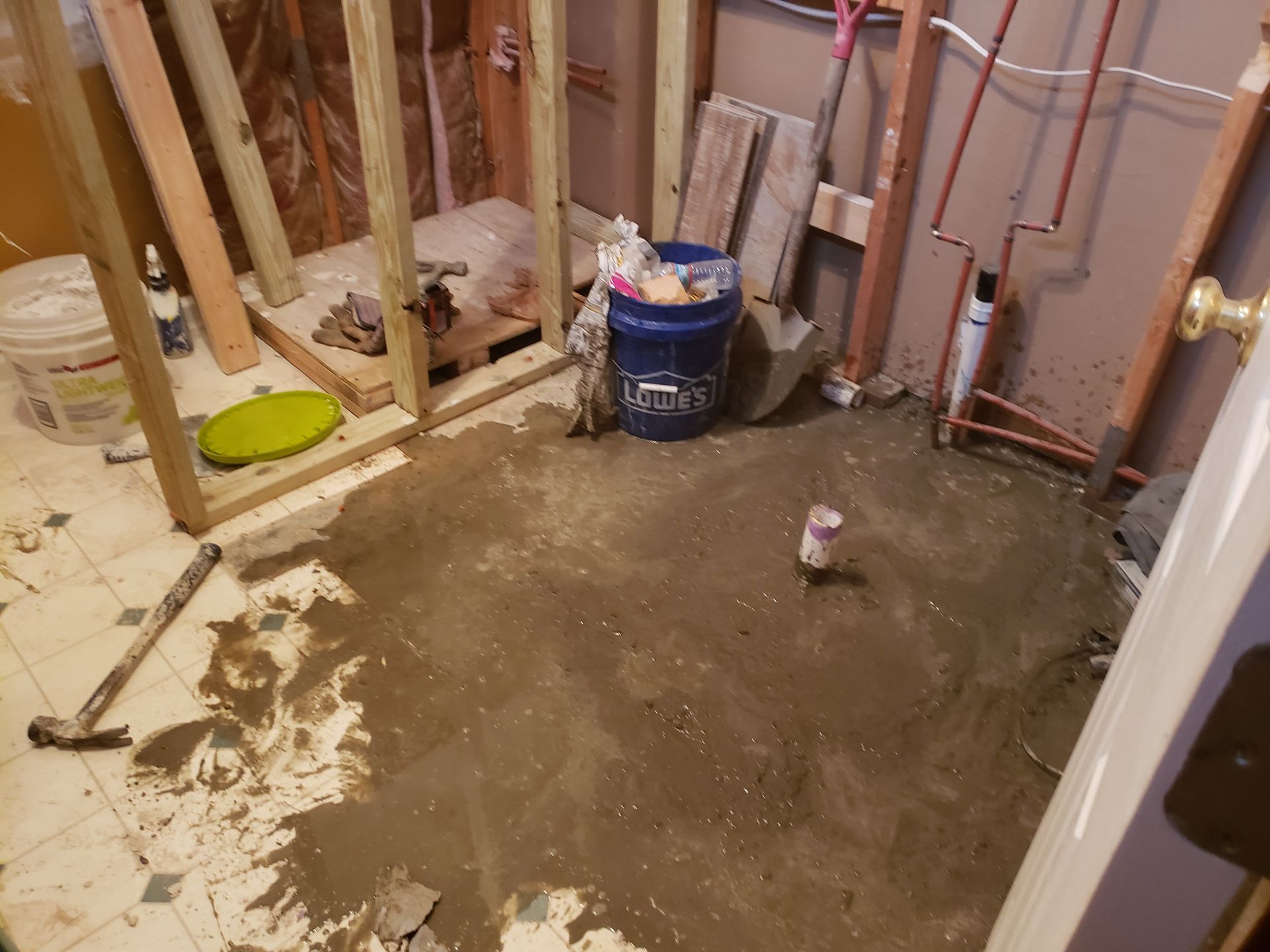 Bathroom under construction with wet concrete floor and exposed framing.