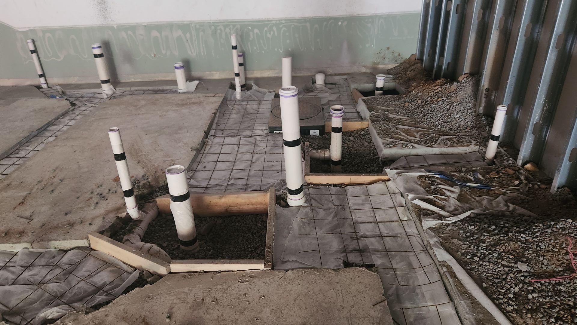 Plumbing work-in-progress: PVC pipes rising from concrete-filled floor sections, in a construction setting.