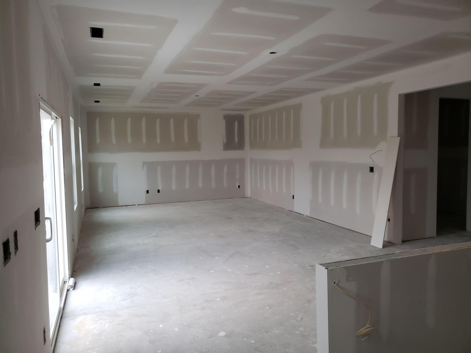 Interior view of a room under construction with drywall installed on walls and ceiling.
