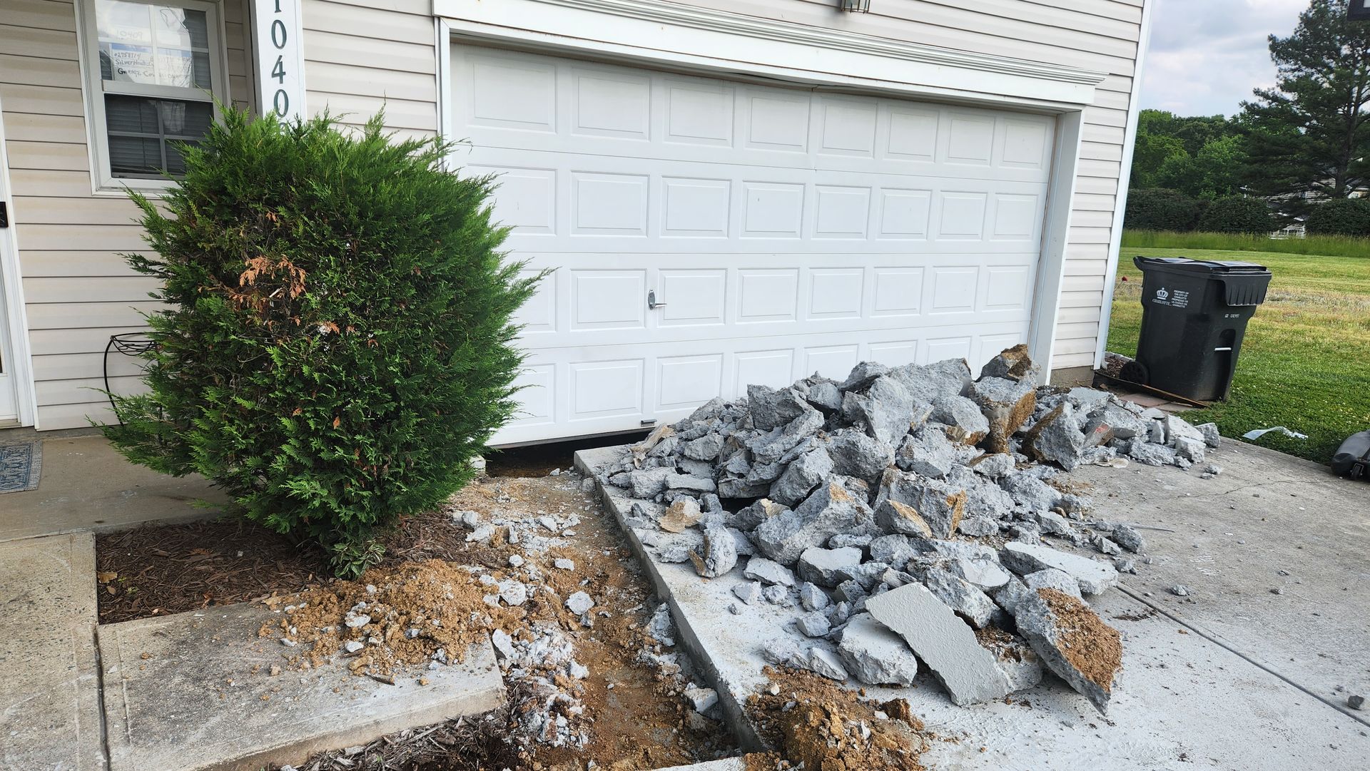 A damaged concrete driveway with a pile of broken pieces in front of a white garage door.