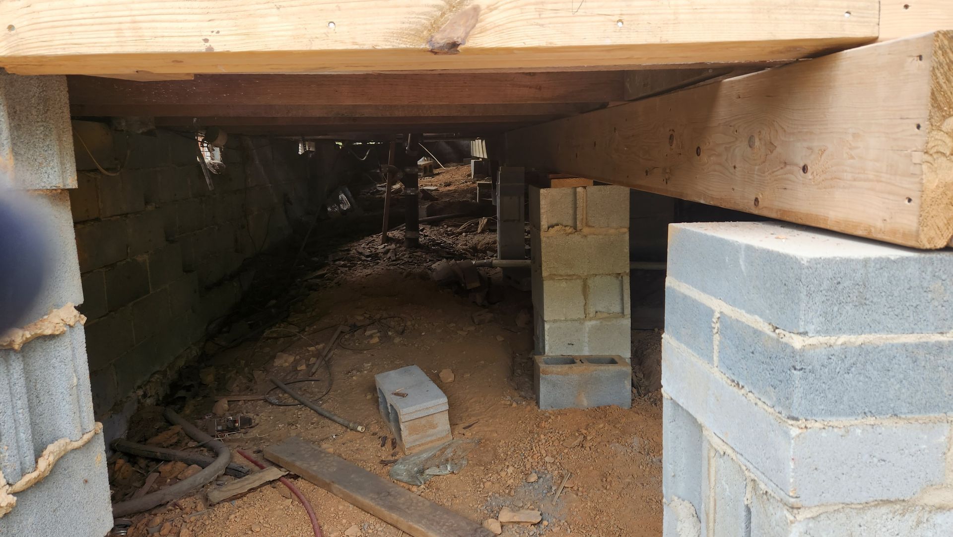 Crawl space under a house with exposed support beams and cinder block pillars.