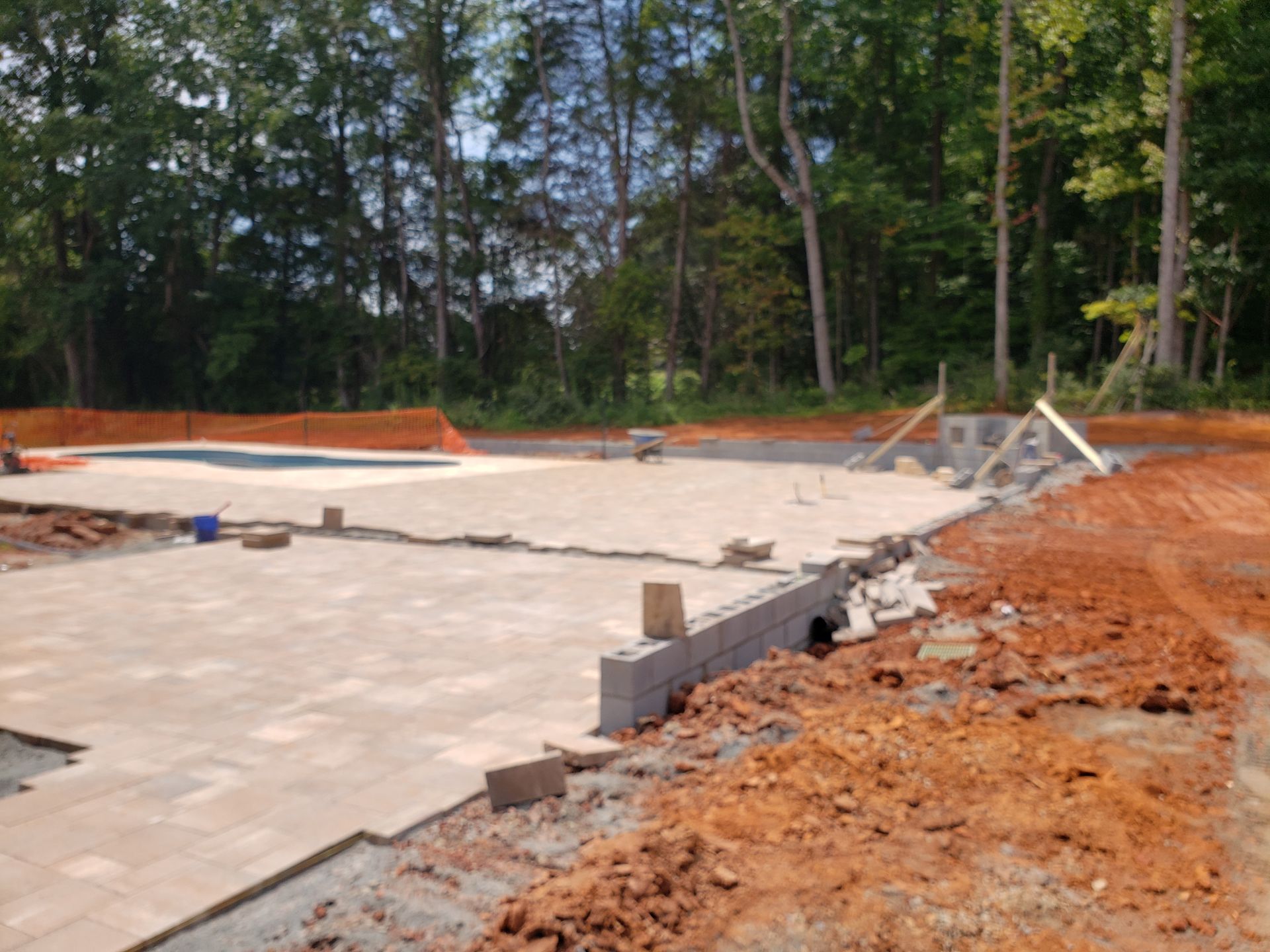 A construction site with a pool in the background and trees in the background.