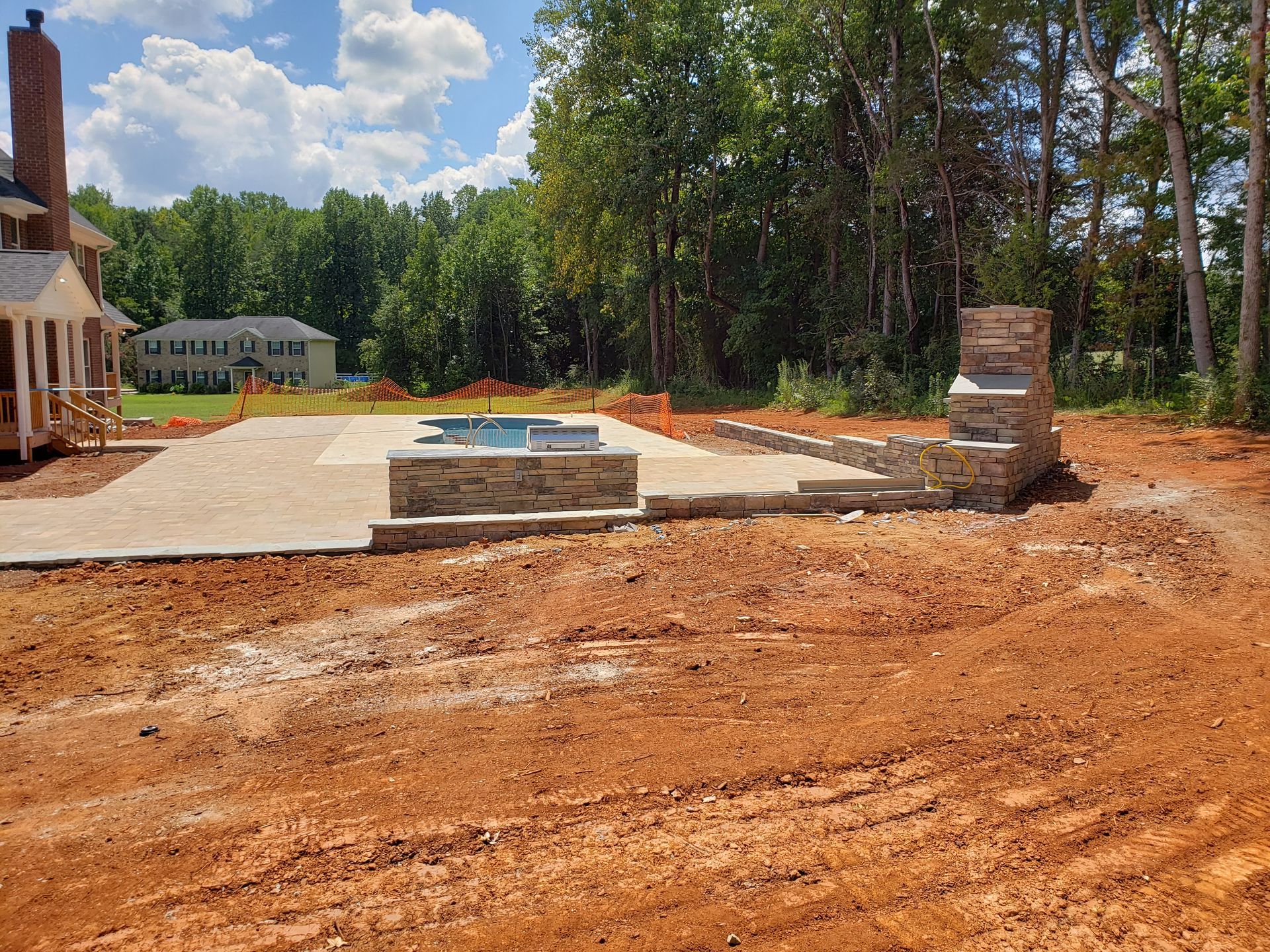 A large dirt field with a house in the background and a swimming pool in the middle.