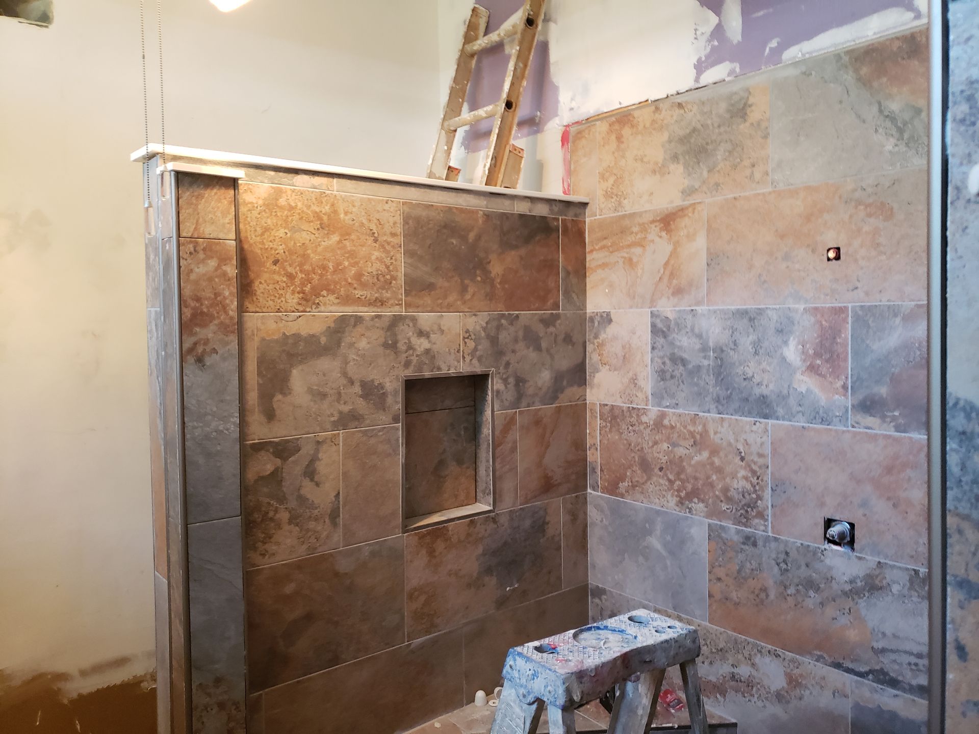 Shower under construction with tiled walls, a built-in niche, and a ladder in the background.