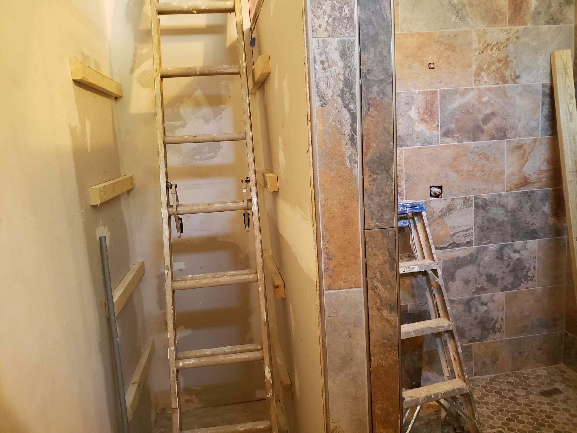 A ladder propped against a wall in a room with stone tiles and wood.