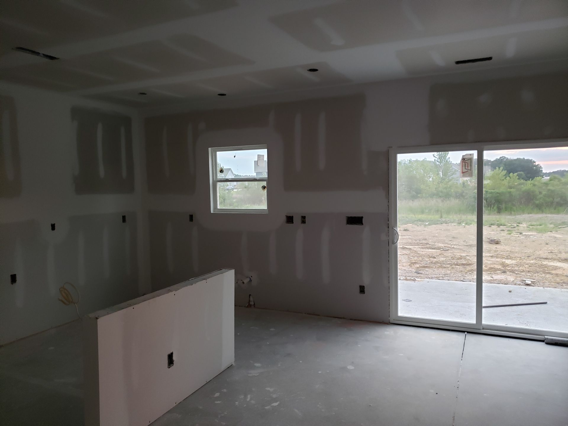 Interior room under construction with drywall installed on walls and ceiling. Sliding glass door, window, and unfinished floor.