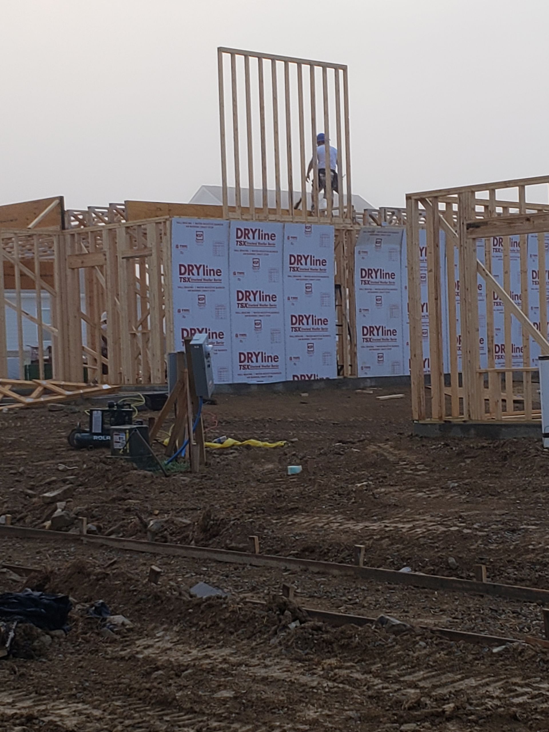 Construction site with a worker on a wooden frame wall. Brown dirt and wooden structures.