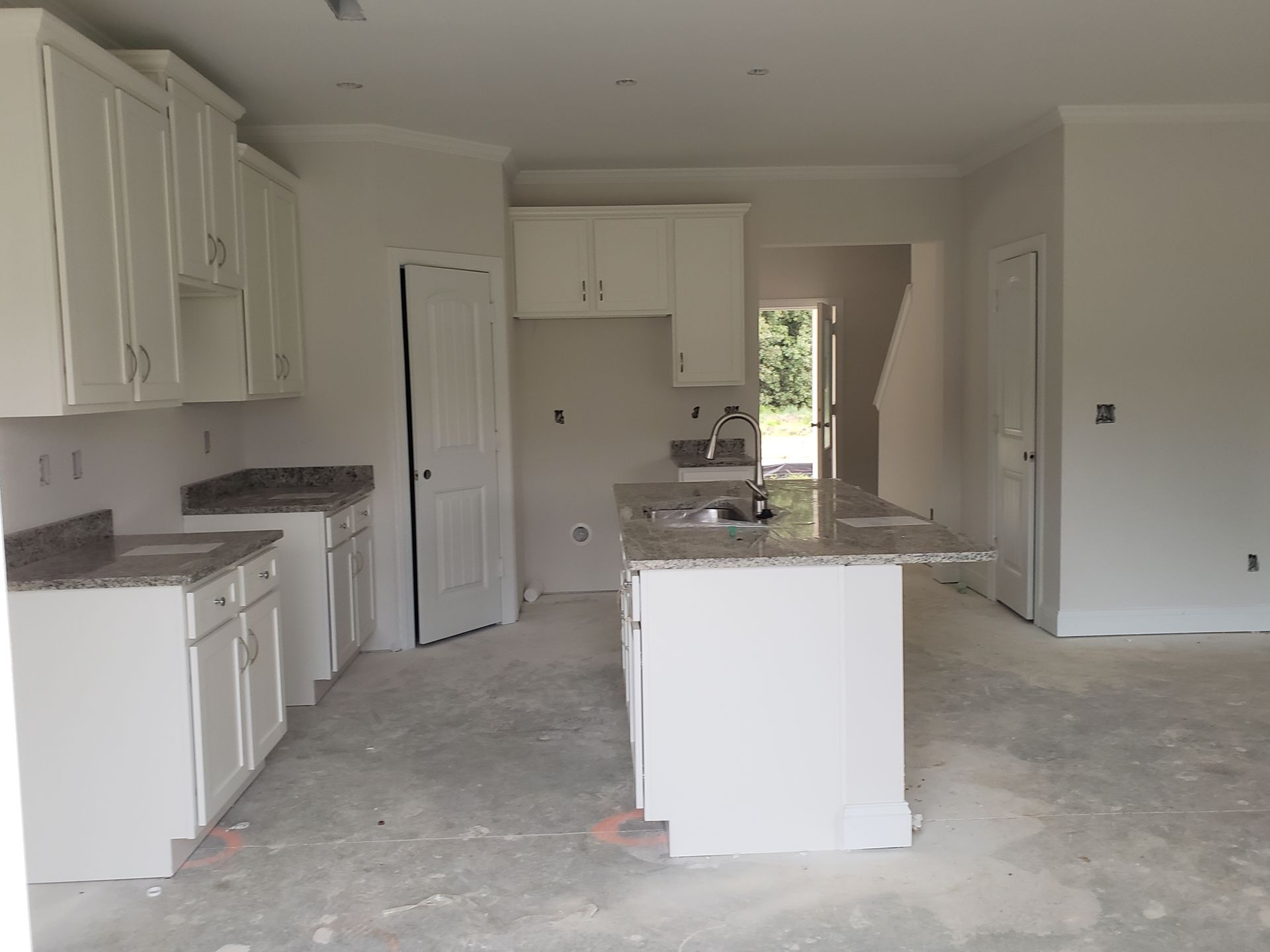 White kitchen with granite countertops, cabinets, and island in a room under construction.