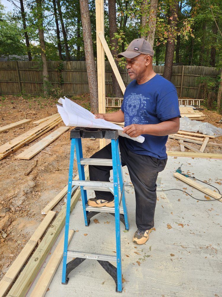 Man in blue shirt and cap, reading plans on a step ladder at a construction site.