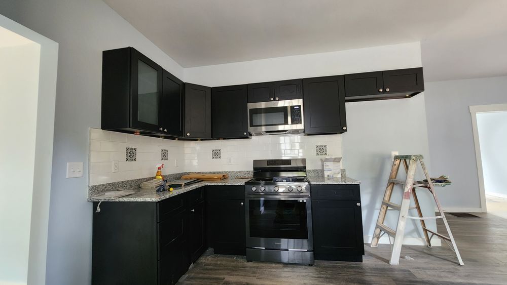 Black kitchen cabinets, stainless steel appliances, and a gray countertop in a newly renovated room.
