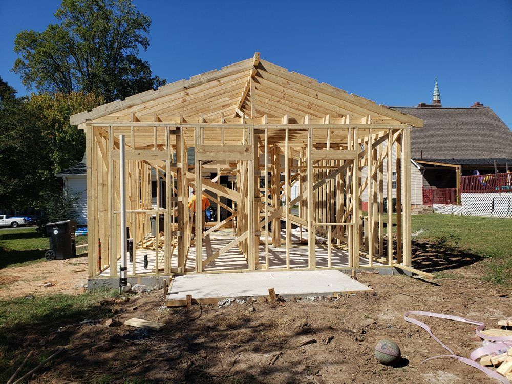 Wooden framework of a building under construction on a concrete foundation, with a blue sky background.