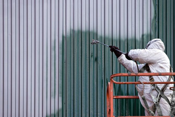 a man in a white coverall spray painting a building