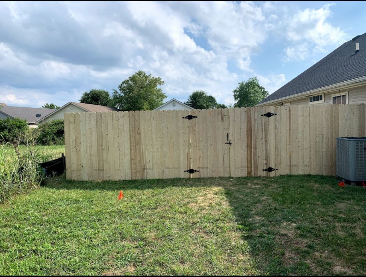 Wooden fence with a gate in a grassy backyard on a cloudy day.