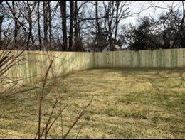 A wooden fence encloses a grassy yard, with trees in the background.