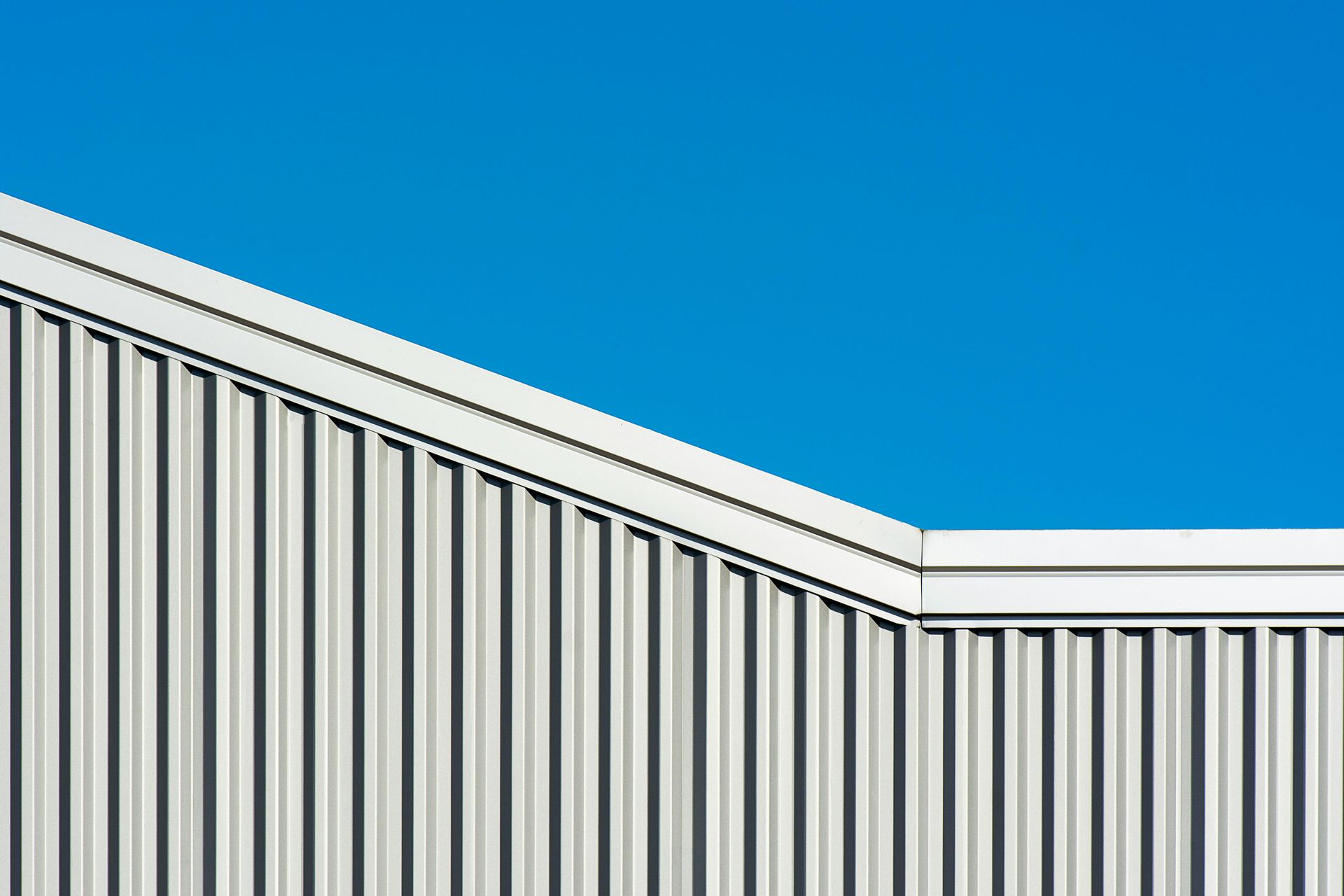 White industrial building with vertical siding against a bright blue sky.