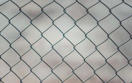 Chain-link fence with a diamond pattern against a blurry, neutral background.