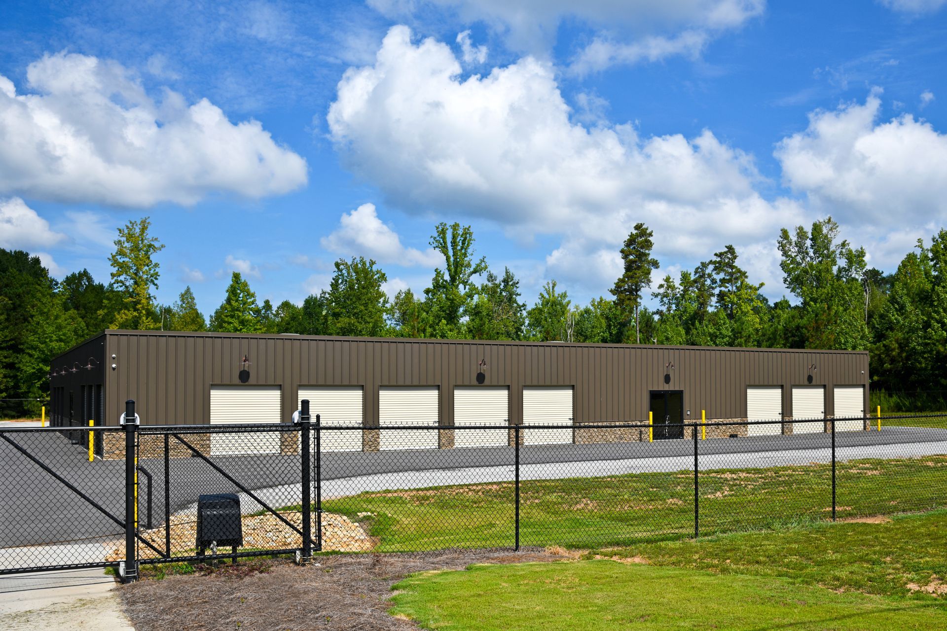 Brown metal storage facility behind a black chain-link fence under a blue sky.