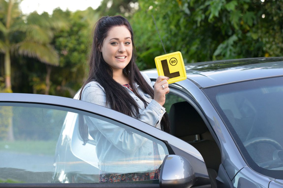 A woman is sitting in a car holding a yellow l sign.