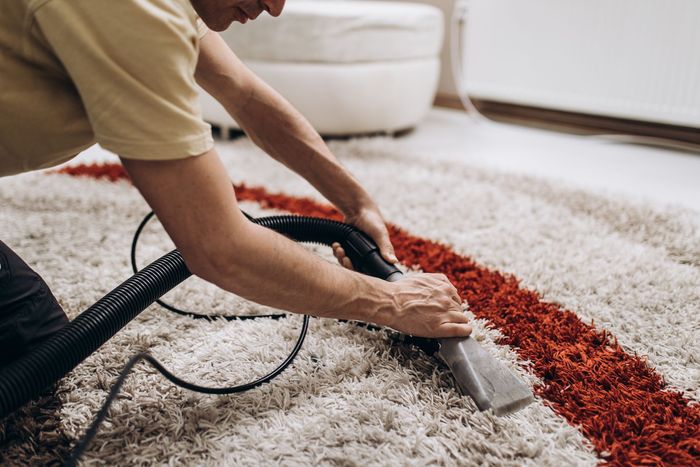 A man is cleaning a rug with a vacuum cleaner.